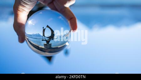 A person's hand holding a crystal ball with a sculpture near lake inside with a blurred background Stock Photo