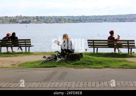 A young woman with a bicycle reading a book in downtown Vancouver, British Columbia, Canada Stock Photo