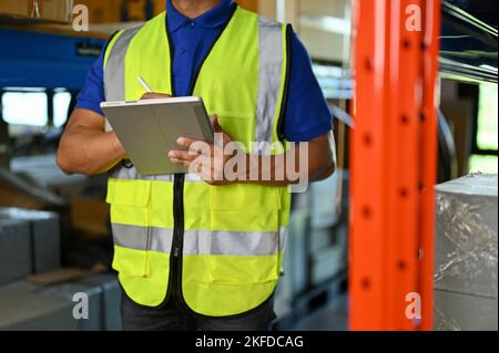 cropped shot, Professional Asian warehouse worker or foreman in uniform checking inventory list on his tablet, working in warehouse. Stock Photo