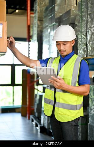 Portrait, Concentrated and professional millennial Asian male warehouse worker using digital tablet to check and manage his inventory, working in ware Stock Photo