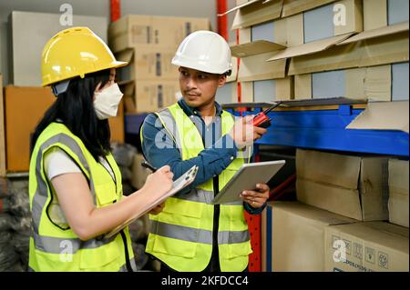 Professional adult Asian male warehouse supervisor training a new female worker, working together in warehouse or storehouse. Stock Photo