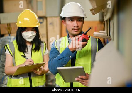 Professional adult Asian male warehouse supervisor and female worker are checking their inventory in the warehouse or storehouse. cargo, shipping indu Stock Photo