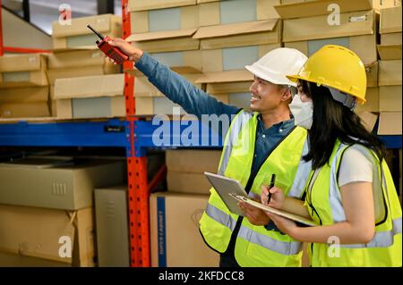 Professional adult Asian male warehouse manager and female worker are working together, checking their inventory in the warehouse or storehouse. Stock Photo