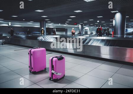 Selective focus on two pink luggage travel wheeled suitcases next to the baggage conveyor belt in an arrival zone of an airport terminal and people wa Stock Photo