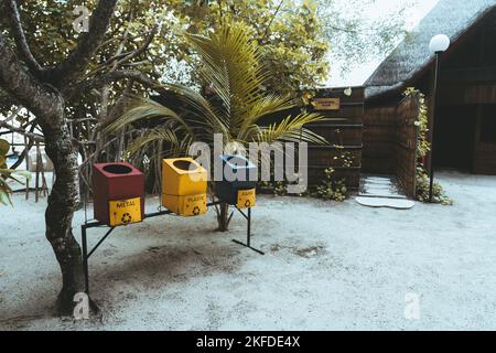 A wide-angle shot of three trash containers for separate waste collection in a luxury hotel in a tropical setting near a changing room: a red one for Stock Photo