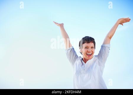 Playful woman enjoying freedom. Playful mature female enjoying freedom against sky with hands outstretched. Stock Photo