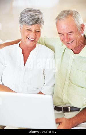 Cheerful couple using laptop at home. Cheerful mature couple using laptop while relaxing at home. Stock Photo