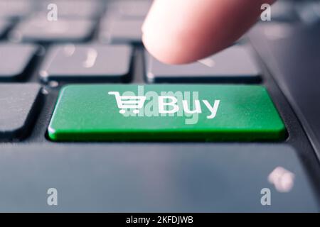 Close-up Of Hand Over Shopping Cart Symbol Button On Keyboard. basket on the keyboard button close up, green button buy. Stock Photo