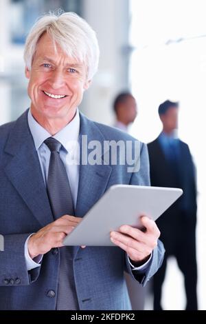 Senior male executive using tablet PC. Portrait of senior male executive using tablet PC with executives in background. Stock Photo