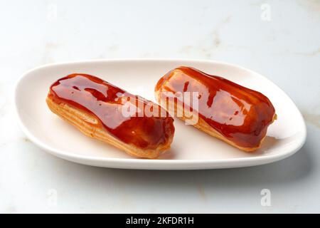 Two caramel eclairs on a white plate Stock Photo
