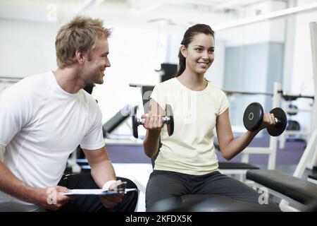 Youre doing a great job so far. an attractive young woman weight training with her personal trainer. Stock Photo