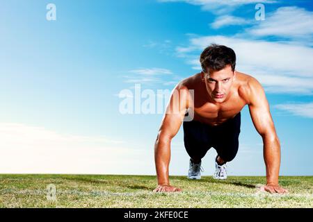 Young man doing pushups on the field - Copyspace. Portrait of a young man doing pushups on the field against the sky. Stock Photo