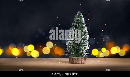 Little Christmas Tree on wood, against dark defocused lights background. Stock Photo