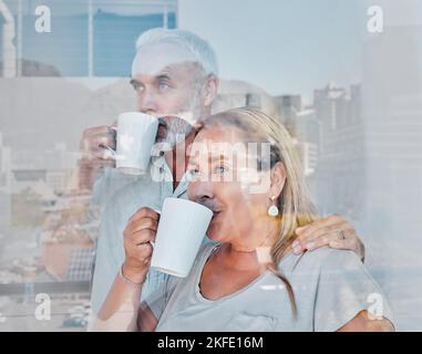 Elderly couple, hug and drinking coffee by window of the city with a vision for morning routine at home. Senior man and woman relaxing looking out Stock Photo