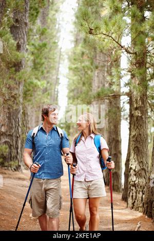Hiking couple smiling and looking at each other. Couple looking at each other and smiling while walking in the woods with backpack and hiking poles. Stock Photo