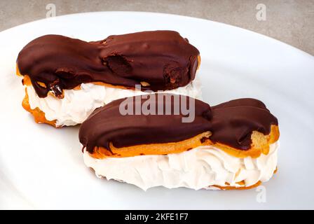 two freshly made chocolate eclairs on white plate with copy space Stock Photo