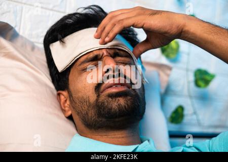 close up head shot of young indian sick man suffering from fever while sleeping at night by placing wet cloth on forehead - concept of healthcare Stock Photo