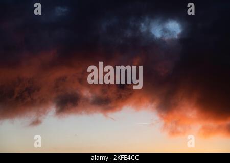 Dramatic sunset skies with orange and black clouds and a plane flying Stock Photo