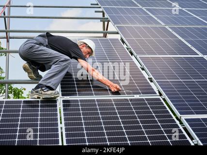 Worker installing solar panel on metal beams at sunny daytime. Renewable and ecological energy. Idea of environment safe. Modern technology and innovation. Man wearing workwear and helmet Stock Photo