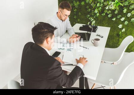Young office worker sitting at desk, using computer. Two business man talking Stock Photo