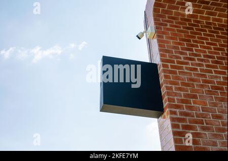 Empty shop signage with CCTV security camera hanging on brick wall and blue sky Stock Photo