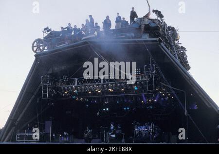 ARCHAOS CIRCUS GROUP, GLASTONBURY 90: Contemporary French circus group Archaos sit on the roof of The Pyramid Stage as The Cure play their headline set at sunset at Glastonbury, Saturday June 23, 1990. This incarnation of the Pyramid Stage burnt down in 1994. Photograph: ROB WATKINS.   INFO: Archaos is a French contemporary circus troupe founded in 1986, known for blending traditional circus acts with punk rock and theatrical elements. Their innovative performances, featuring motorbikes, chainsaws, and pyrotechnics, have revolutionized the circus world Stock Photo