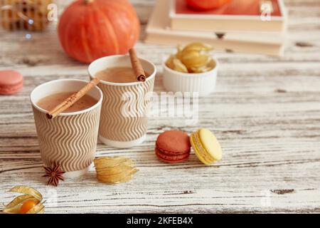 Aesthetics cardboard cups of pumpkin latte and cinnamon sticks among autumn decorations. Seasonal coffee time with macaroons and winter cherry. Cozy a Stock Photo