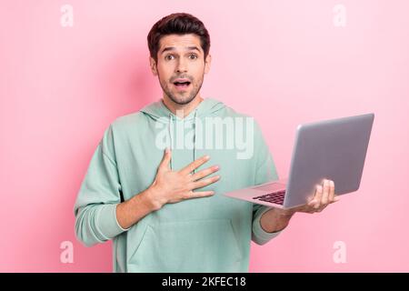 Photo of young upset surprised impressed businessman wear khaki hoodie unexpected reaction his account banned laptop isolated on pink color background Stock Photo