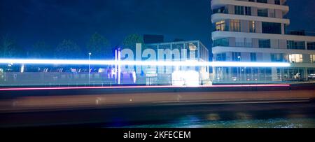 Lighttrails of a boat passing at night throug a city with some buildings in the background Stock Photo
