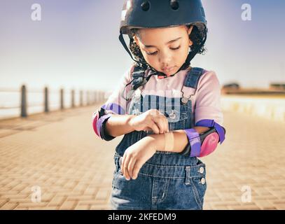 Cycling injury, arm bandage and child in street with bruise after fall or accident. First aid, bandaid and hurt city girl with safety helmet after Stock Photo