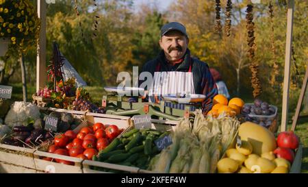 Elderly farmer stands at the stall with fresh colorful fruits and ...
