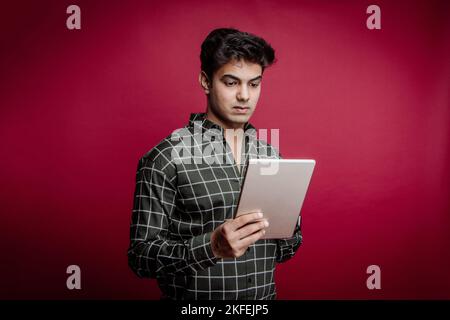 Smiling young Indian businessman, Arab professional, freelancer, jewellery manager, and businessman holding tablet and standing in a studio background Stock Photo
