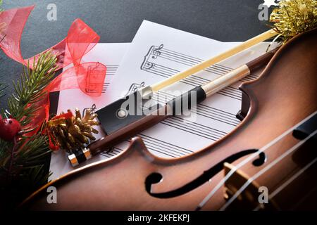 Violin and bow on sheet music on black table with christmas decoration. Elevated view. Stock Photo