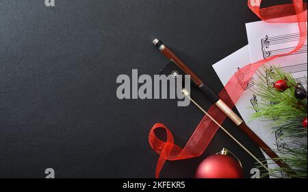 Concept of performance of stringed instruments with bow on sheet music with Christmas decoration on black background. Top view. Stock Photo