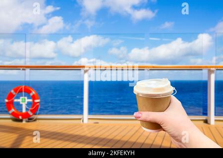 Hand holding paper cup of hot coffee on a deck of cruise ship with ocean on background with copy space