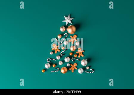 3d illustration of arranged sweet candy canes with gingerbread man cookies and shiny baubles in shape of Xmas tree on green background Stock Photo