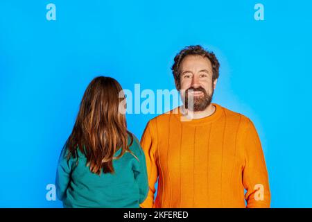 Funny dad with child daughter teen girl with isolated on blue background studio portrait. She does not want photos, no face child. Family day parentho Stock Photo