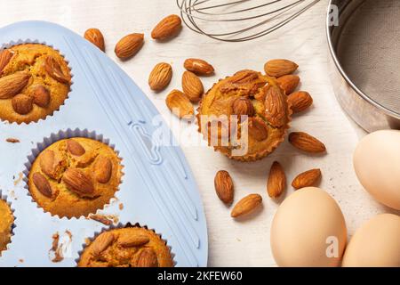 Set of various baking ingredients - flour, eggs, sugar, butter, nuts, kitchen utensils and cupcake baking dish on white background. Top view. Stock Photo