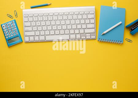 Working yellow table with keyboard, notebook, calculator, pencil, stapler and paper clips. Space for your inscription. Stock Photo