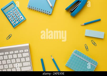 Working yellow table with a keyboard, calculator, notebooks, eraser, pencil, felt-tip pen, stapler and paper clips. Top view with copy space. Stock Photo