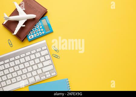 On a yellow desktop, a keyboard, calculator, passport, mock-up of an airplane, a notebook and paper clips. Space for your inscription. Stock Photo