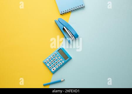On a blue-yellow background is a calculator, notebook, stapler, pencil. Space for your inscription. Stock Photo