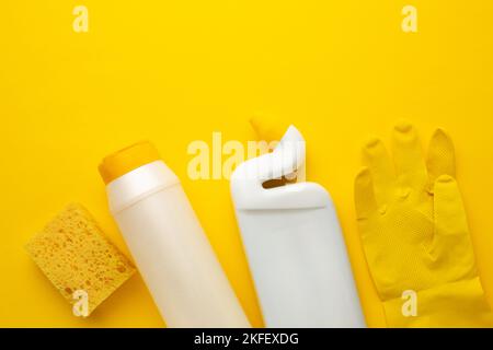 Plastic bottles of cleaning products, sponge and glove on yellow background with space for inscription. Stock Photo