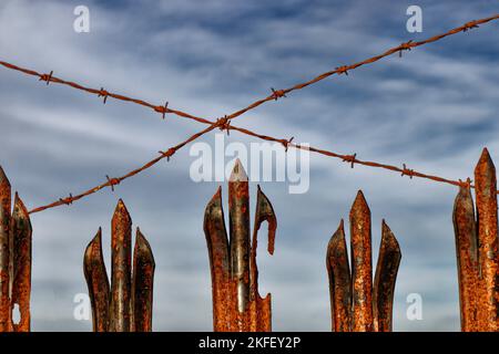 Barbed wire and rusted sharp pointed railings of an old metal fence Stock Photo