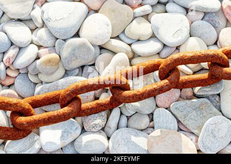 Old rusted textured weathered metal chain and links resting on a pebble beach Stock Photo