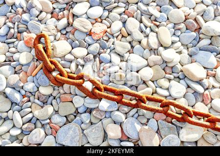 Old rusted textured weathered metal chain and links resting on coloured pebbles Stock Photo