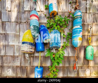 group of assorted buoys hung on the exterior of a cedar shingled building Stock Photo