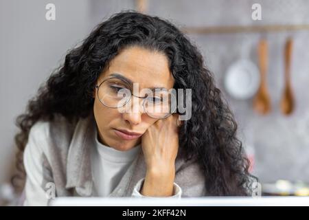 Close-up photo. Young hispanic woman suffering from depression, sitting sad and lonely, holding head with hand, looking down Stock Photo