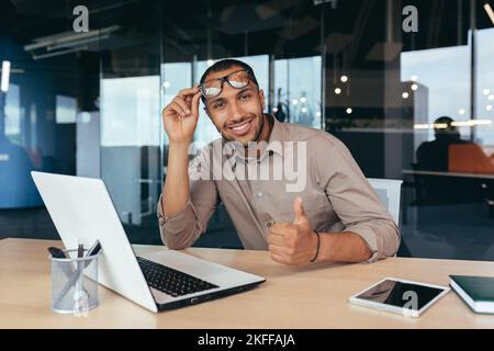 Portrait of programmer in office with laptop African American man looking at camera showing thumb up affirmative. Stock Photo