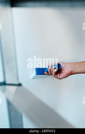 closeup of a man spreading some glue with a brush on a wall before to attach a piece of wallpaper to it Stock Photo